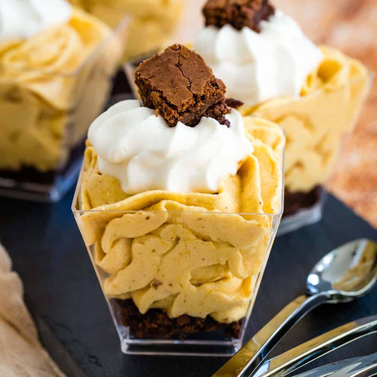 A pumpkin mousse parfait with a brownie base in a mini plastic cup.