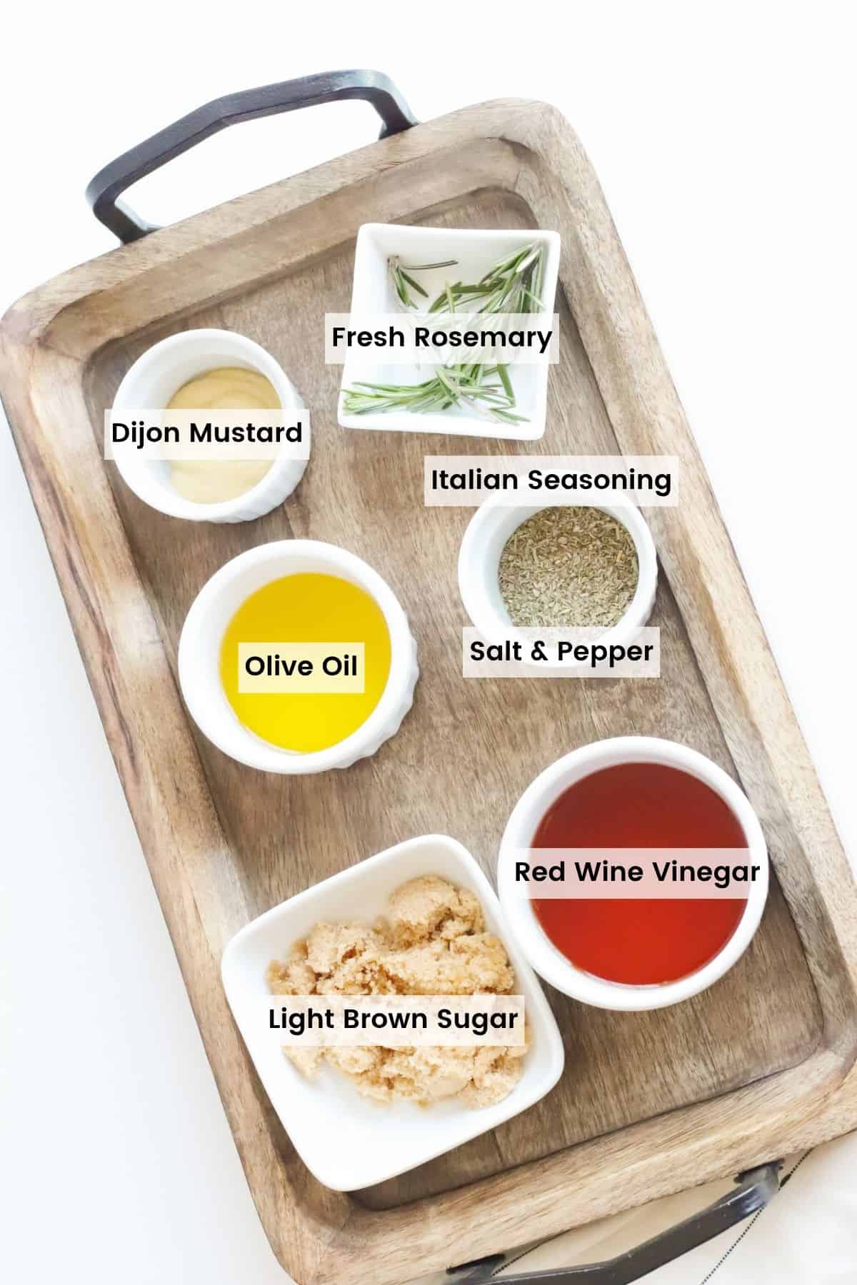 Bowls of red wine vinegar, olive oil, dijon mustard, dried Italian seasoning, brown sugar, and fresh rosemary on a wooden serving tray with text labels.