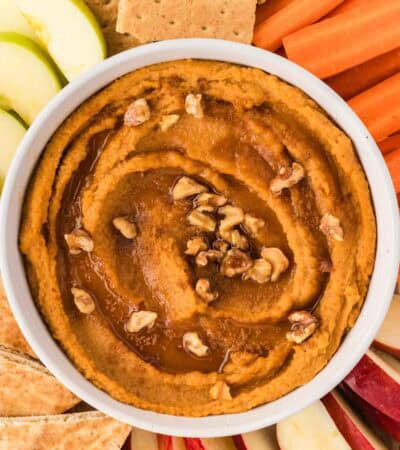 Overhead image of sweet potato hummus topped with maple syrup and walnuts, surrounded by dippables.
