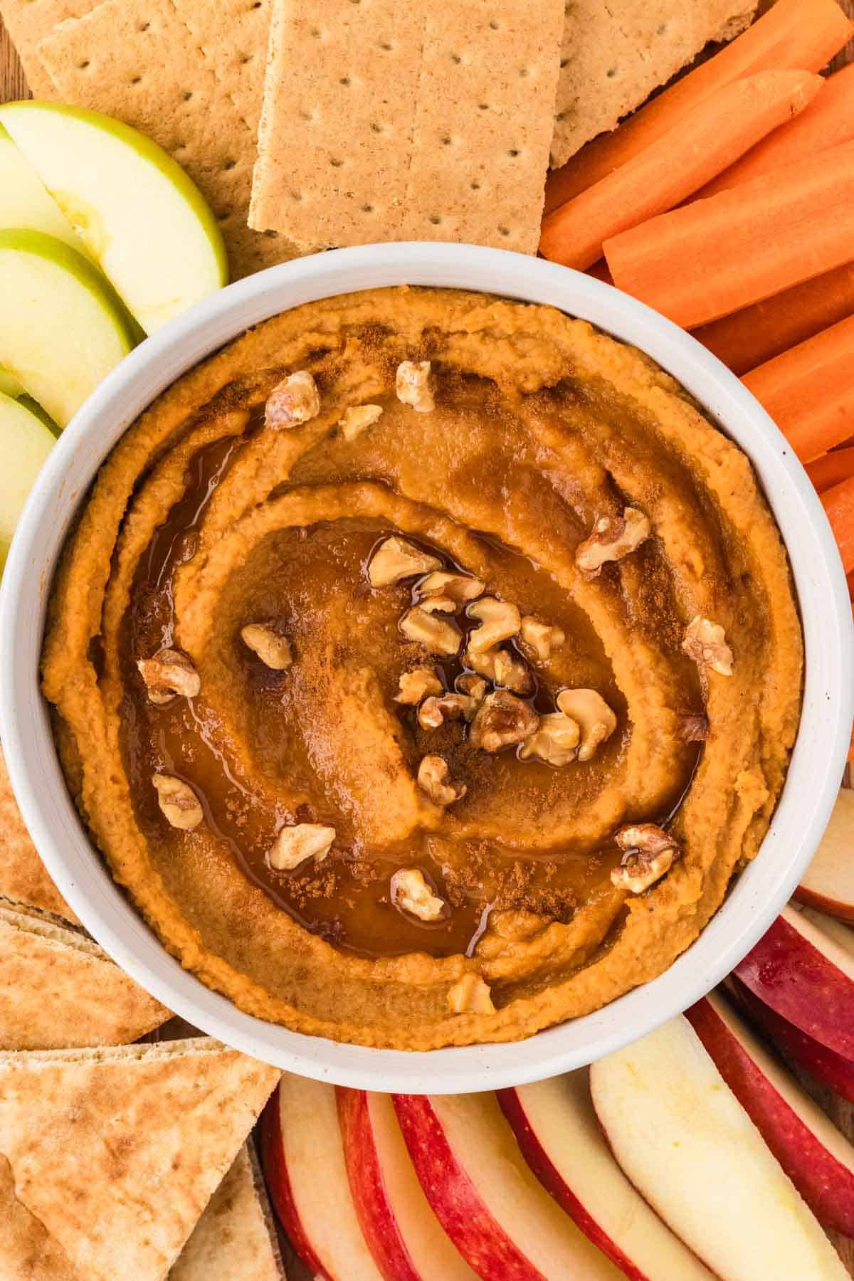 Overhead image of sweet potato hummus topped with maple syrup and walnuts, surrounded by dippables.