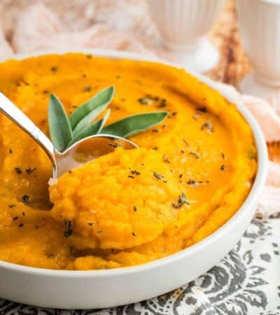 A serving spoon taking a scoop of mashed butternut squash from a bowl.