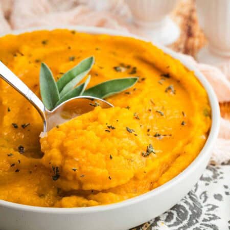 A serving spoon taking a scoop of mashed butternut squash from a bowl.