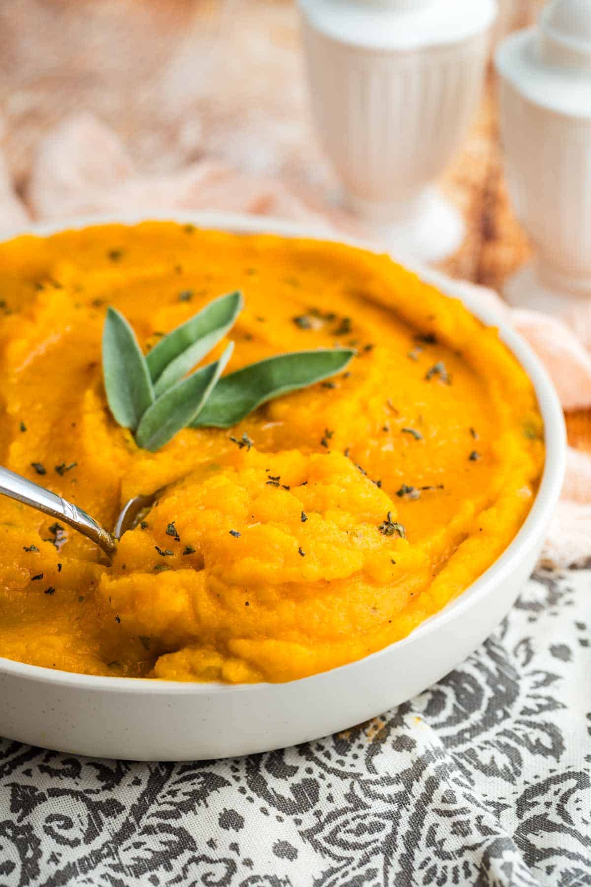 A serving dish full of mashed butternut squash with a serving spoon in it.