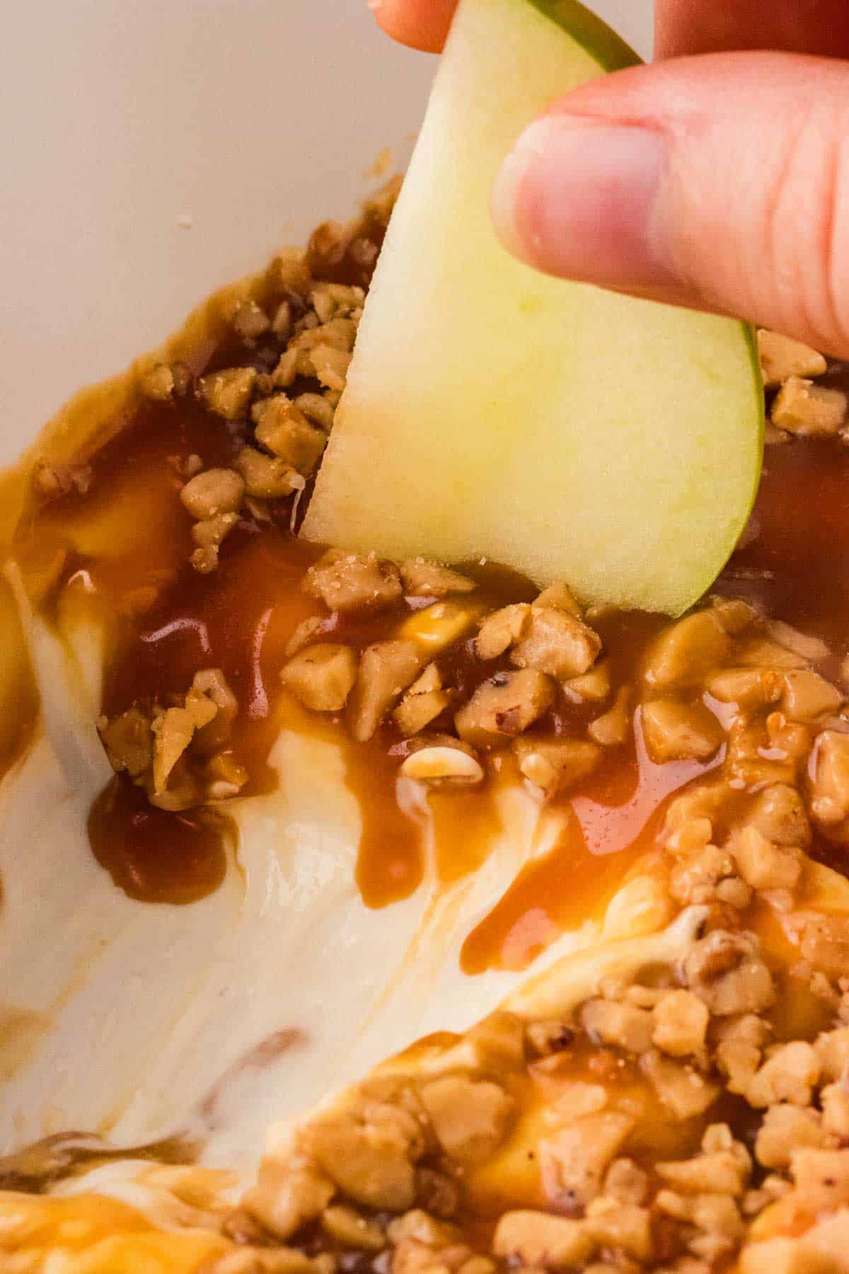 Close-up image of scooping up caramel apple dip with an apple slice.