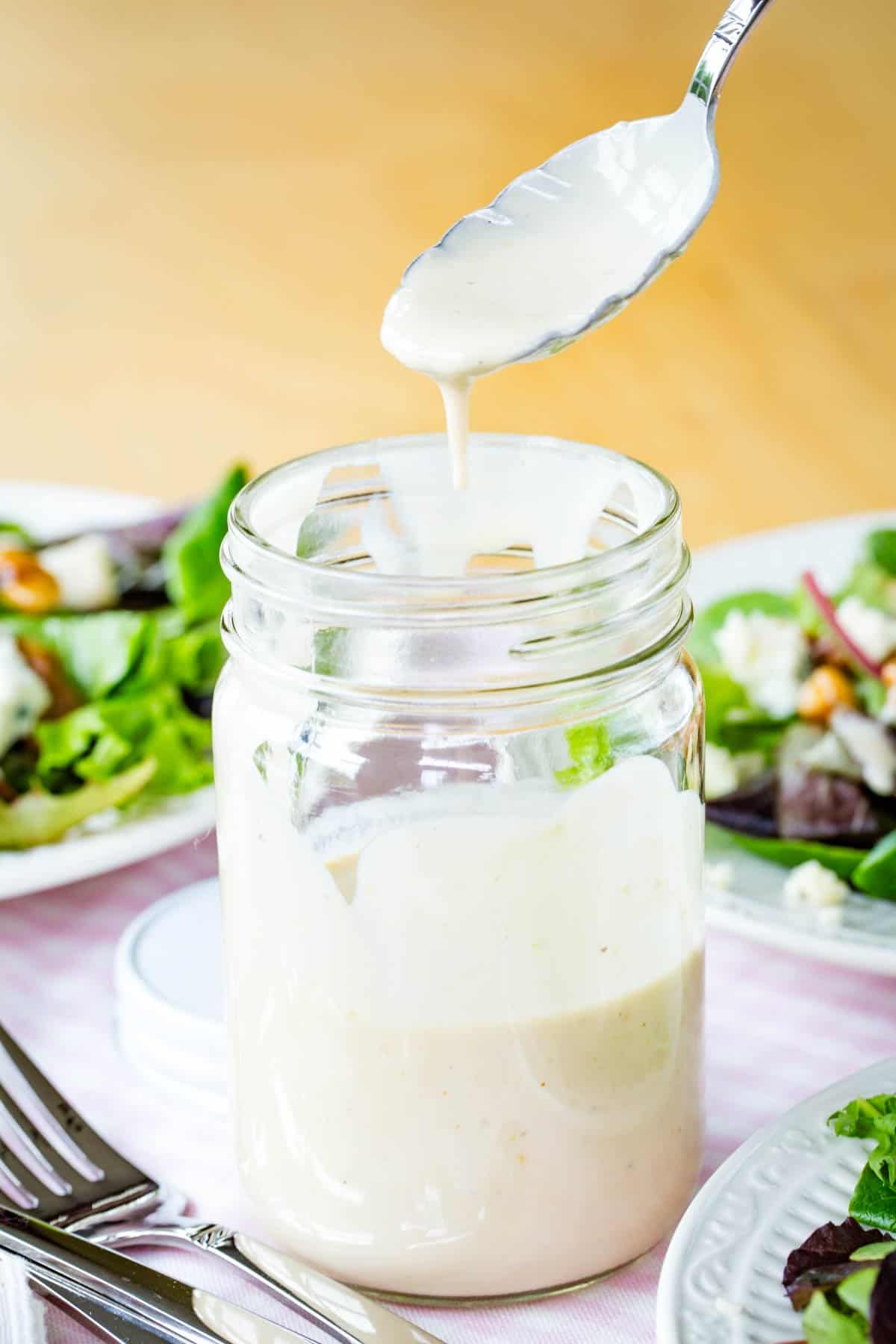 A spoon dipping into a jar of creamy sherry vinaigrette.
