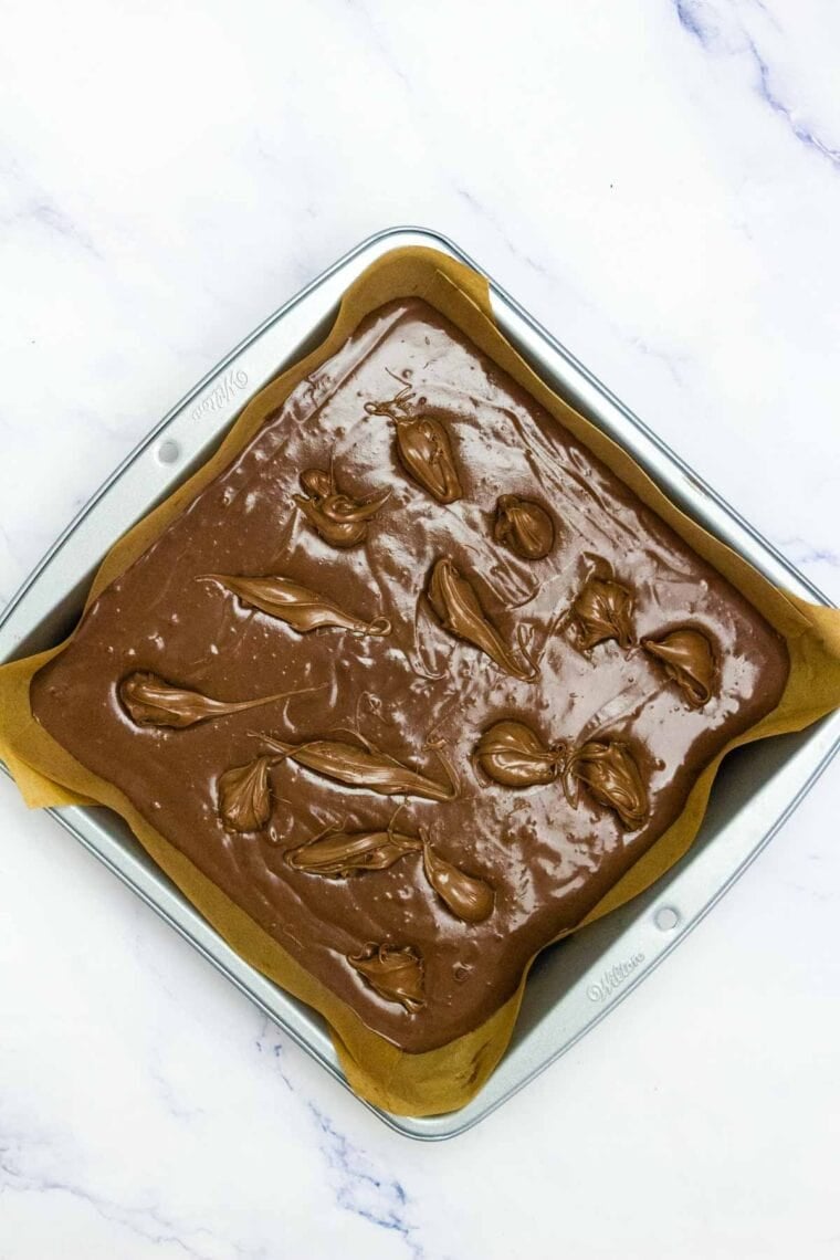 Dollops of Nutella in Nutella brownie batter in a pan.