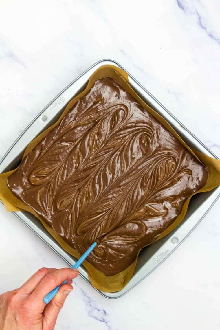 Swirling dollops of Nutella into Nutella brownie batter in a pan.
