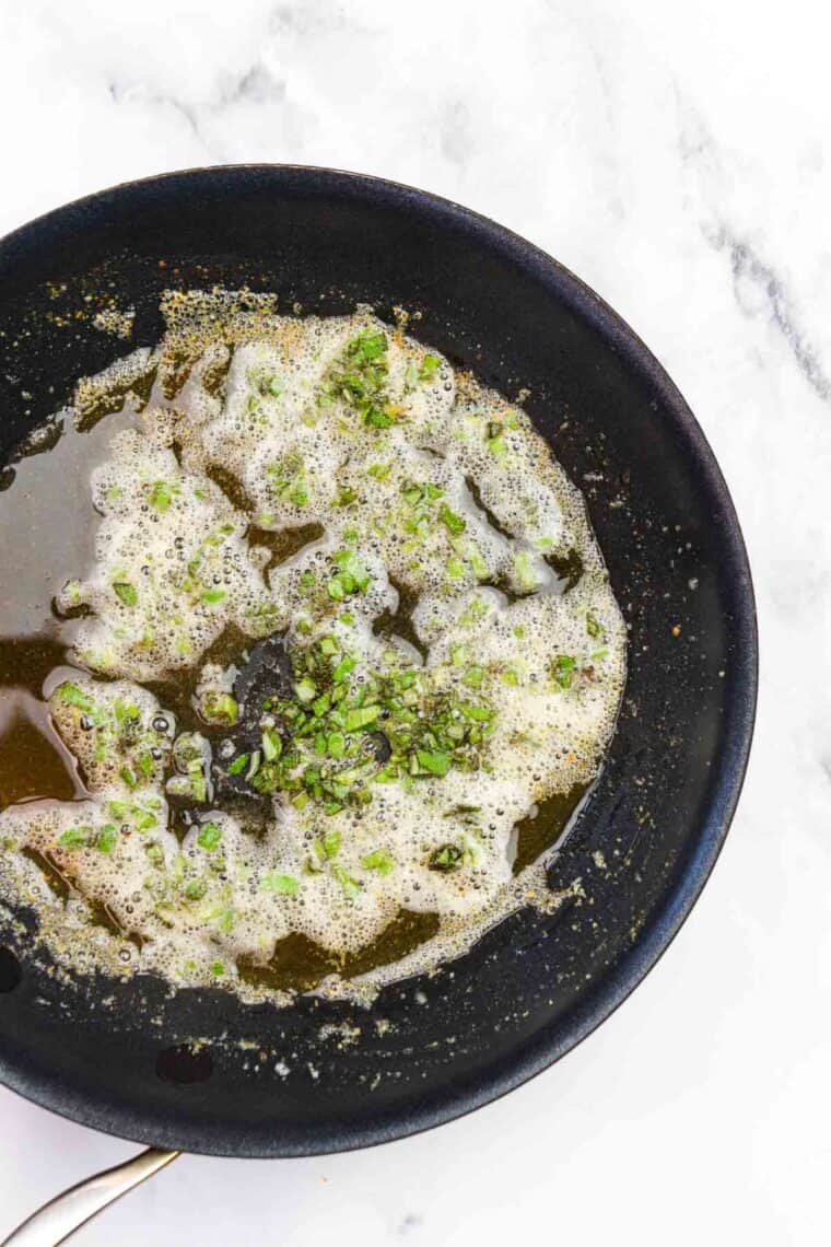 Adding sage to browned butter in a skillet.
