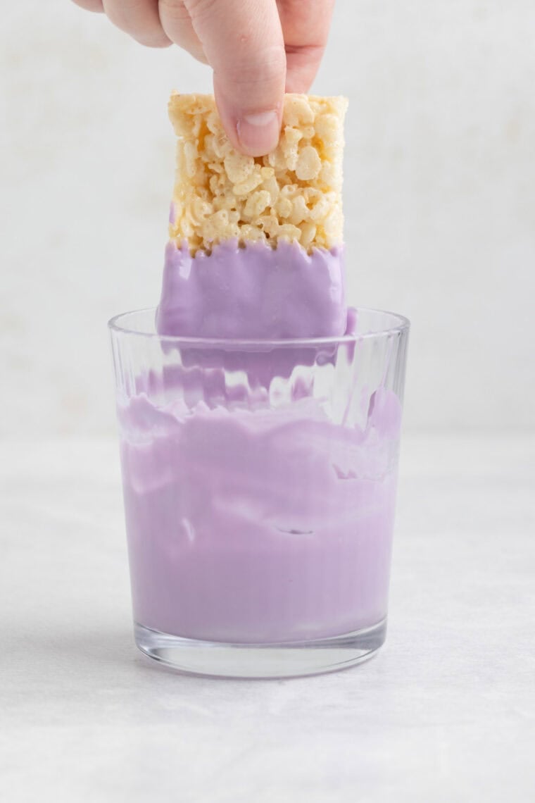 Dipping a Rice Krispies treat into a cup of melted purple candy melts.