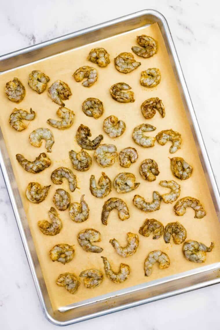 Seasoned shrimp spread over a baking sheet.