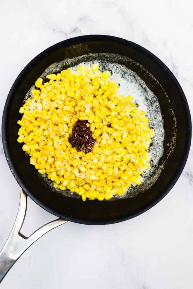 Adding corn and chopped chilis in adobo to a skillet with butter.