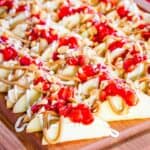 A platter of apple slices topped with cream cheese and peanut butter drizzles and strawberry sauce with text overlay that says "Peanut Butter & Jelly Apple Nachos".