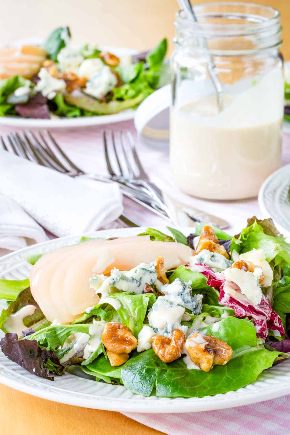A white plate loaded with salad greens, poached pears, honeyed walnuts, and gorgonzola.