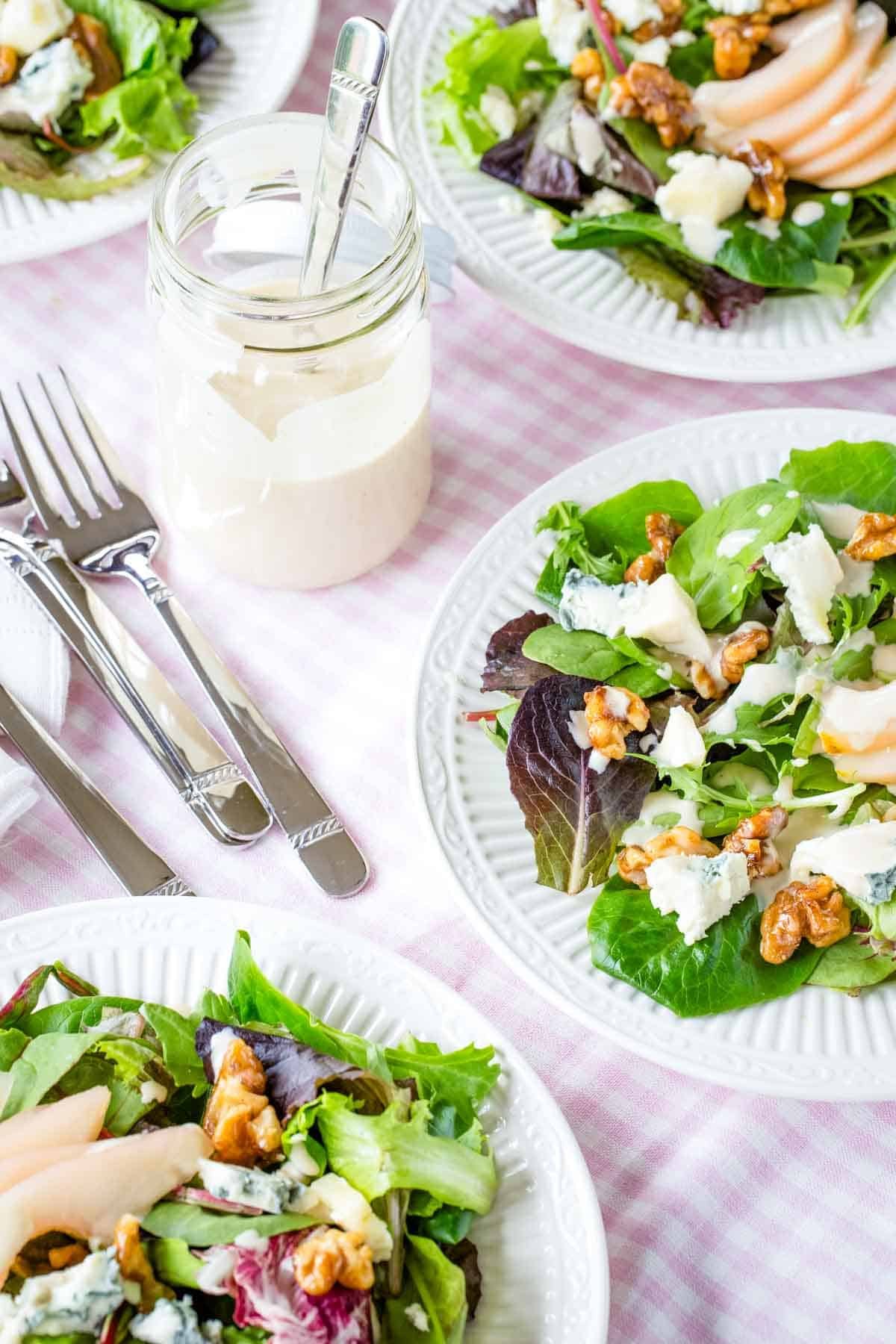 Poached pear salad served on white plates near a jar of sherry vinaigrette.