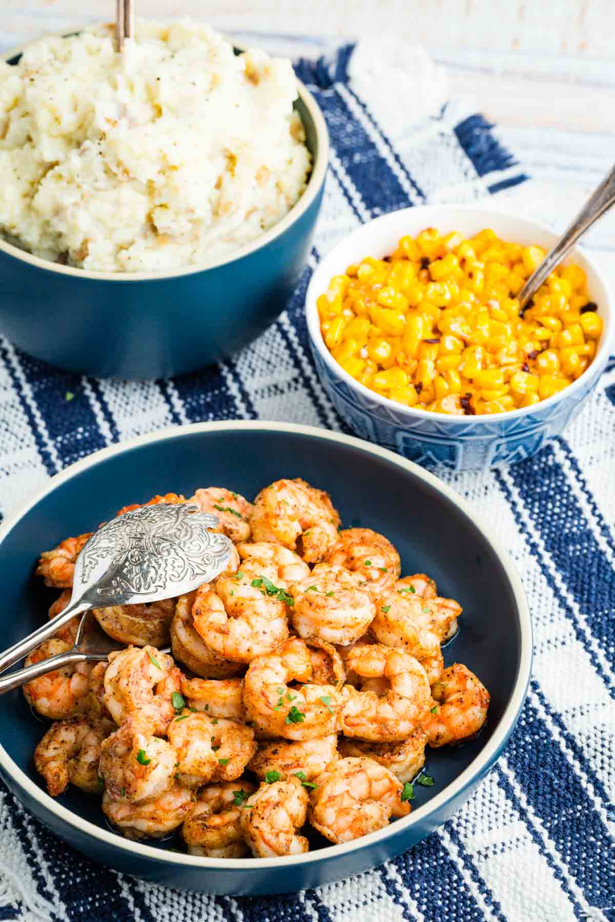 A bowl of shrimp near a bowl of corn and a bowl of mashed potatoes.