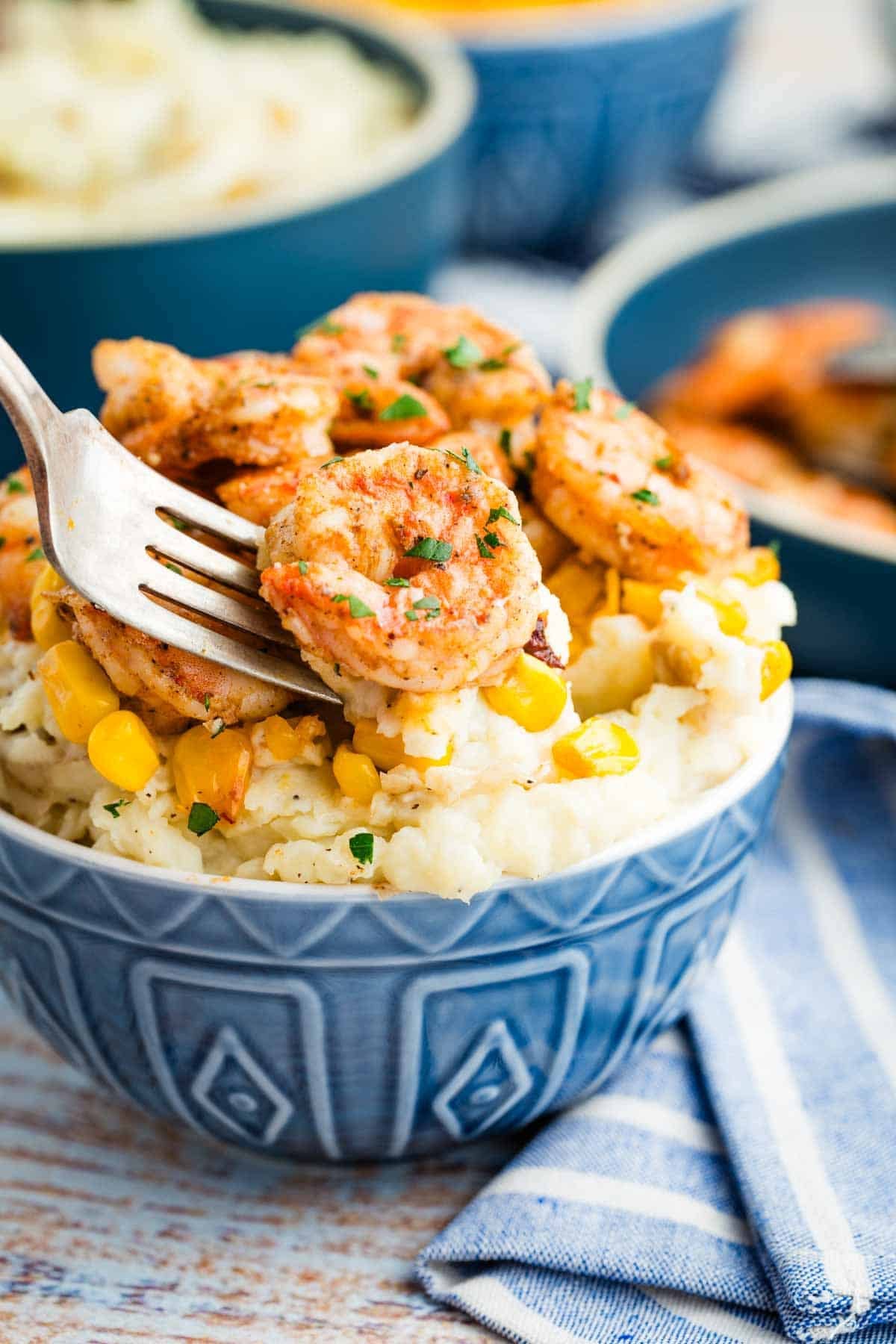 A fork taking a shrimp from a bowl of shrimp and mashed potatoes.