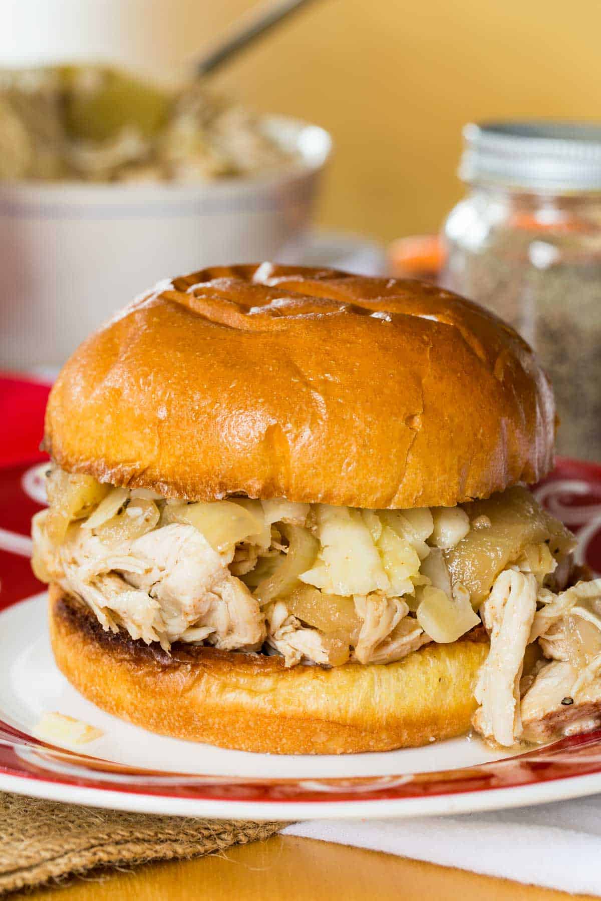 This easy slow cooker pulled chicken is simmered for hours with hard apple cider, apples, and onion. It's SO tender and ideal for sandwiches! A closeup of a apple cider pulled chicken sandwich.