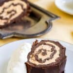A slice of a chocolate cake roll with pumpkin mousse filling on a plate with text overlay that says "Flourless Chocolate Pumpkin Roll".
