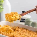 A scoop of macaroni and cheese being lifted from the casserole dish on a wooden spoon with text overlay that says "Gluten Free Baked Mac & Cheese".