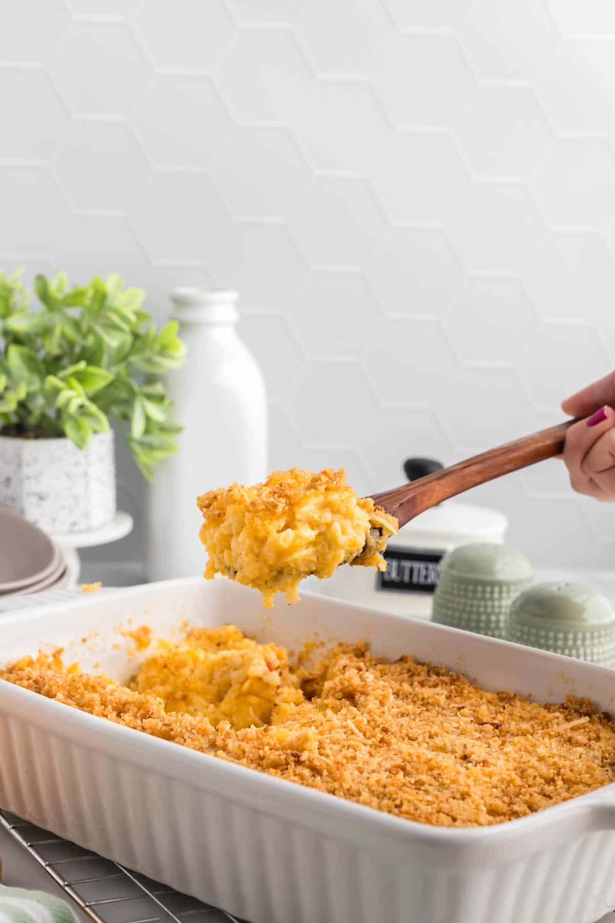 This gluten-free mac and cheese is so creamy and satisfying, with a crunchy breadcrumb topping that takes it over the edge! A wooden spoon scooping some gluten free mac and cheese out of a casserole dish.