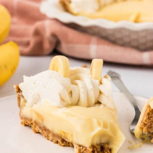 A slice of gluten free banana cream pie on a plate with a bite taken out of it.