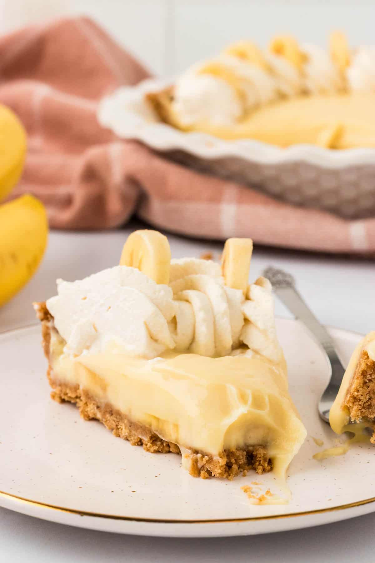 A slice of gluten free banana cream pie on a plate with a bite taken out of it.