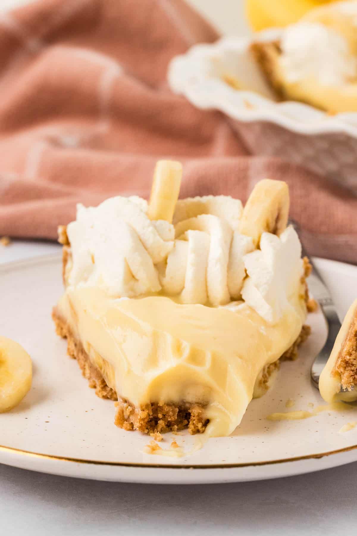 Close-up image of a slice of gluten free banana cream pie on a plate with a bite taken out of it.