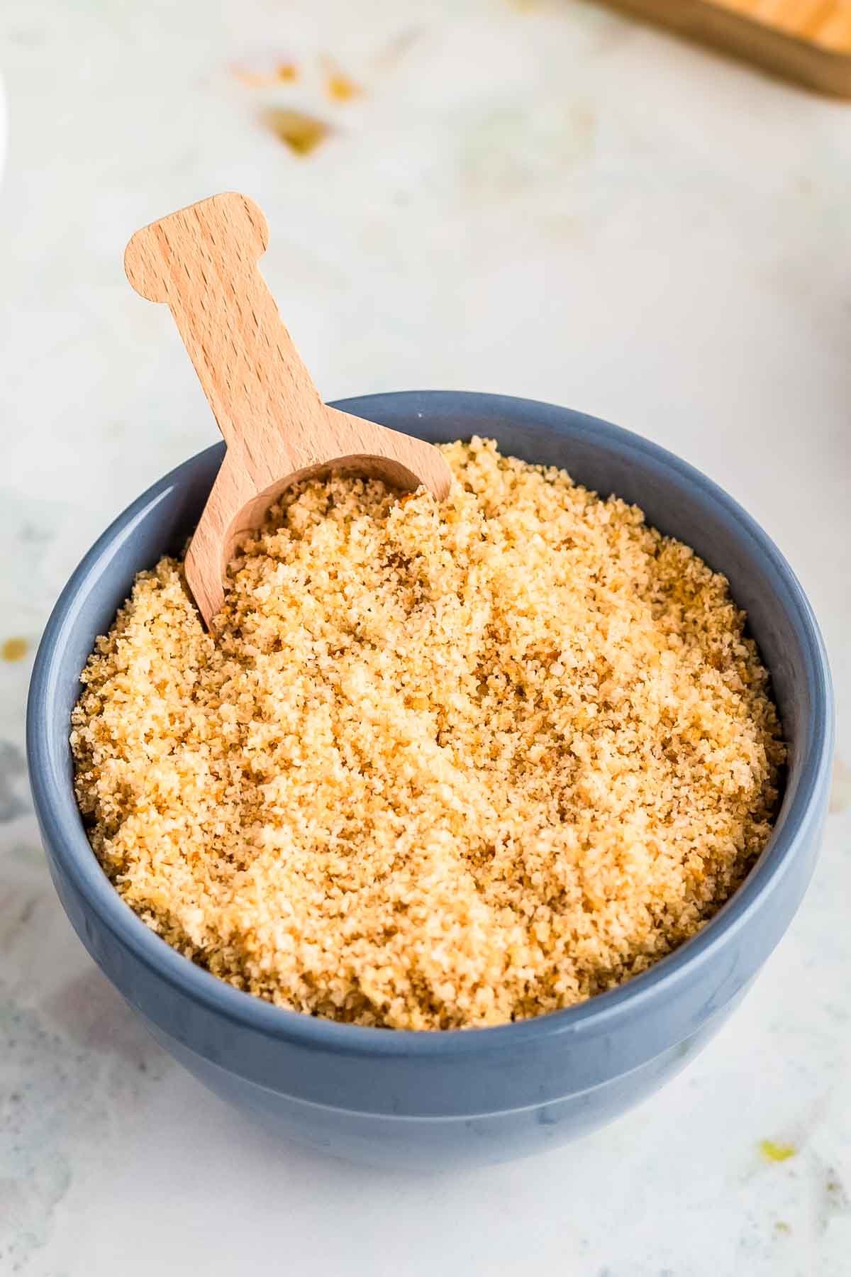 Gluten free breadcrumbs in a bowl with a wooden scoop.