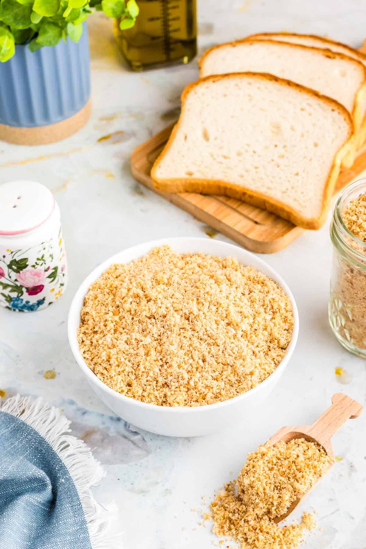 Gluten free breadcrumbs in a bowl with sliced bread behind it.