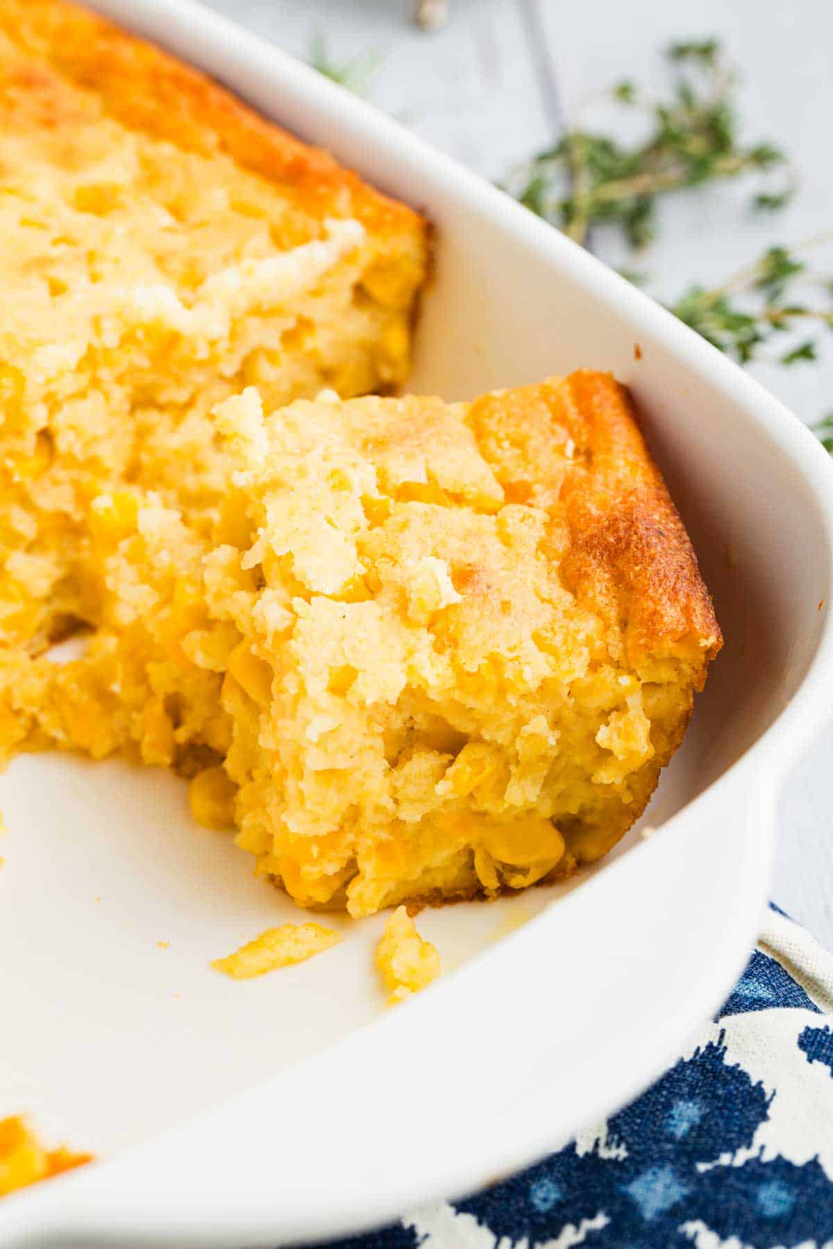 This wildly easy gluten-free corn casserole combines sweet and savory goodness with a creamy texture that’s guaranteed to be a hit. A slice of corn casserole in the corner of a baking dish.