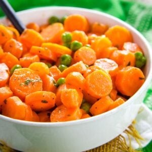 A bowl of carrots and peas with a serving spoons.