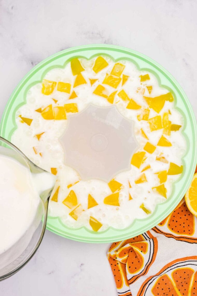 Pouring vanilla ice cream "jello" mixture over cubes of orange jello in a jello mold.