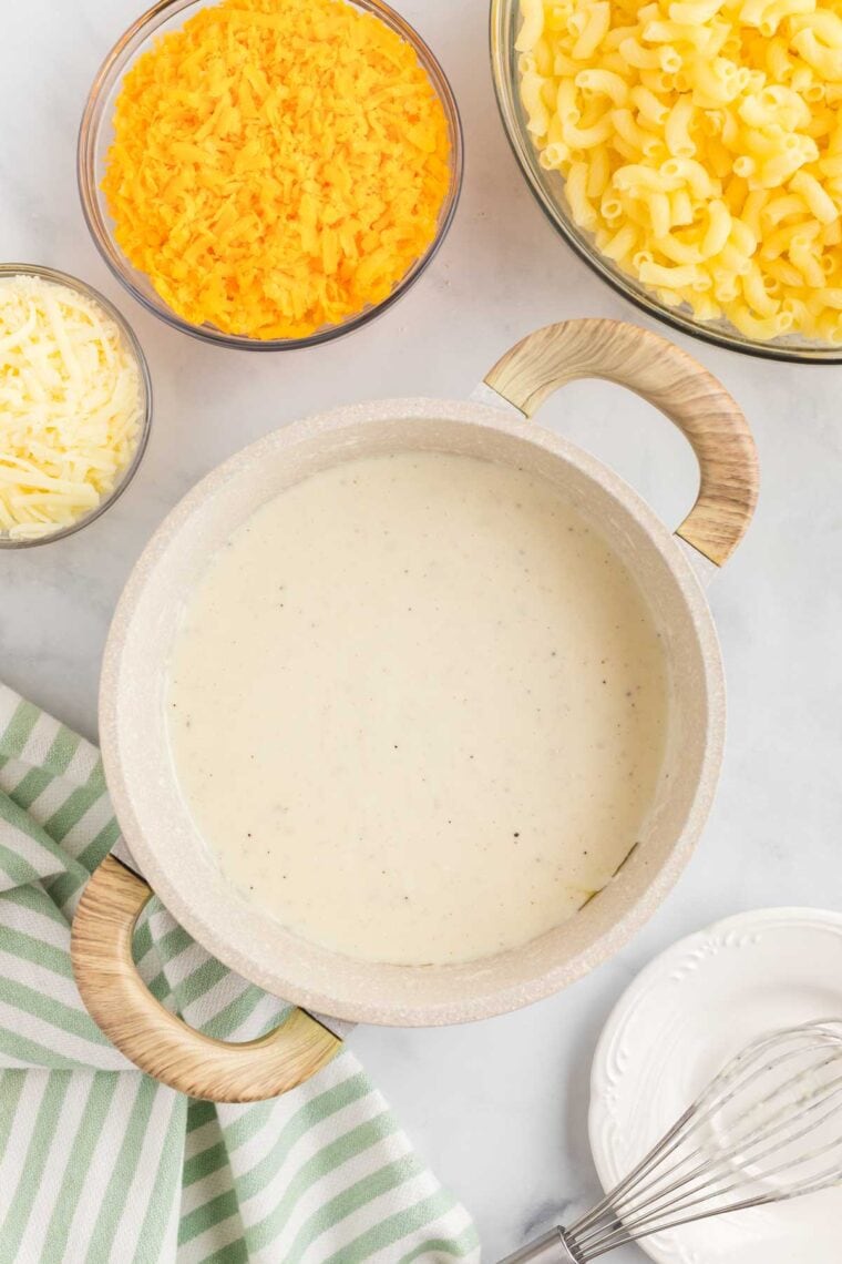 This gluten-free mac and cheese is so creamy and satisfying, with a crunchy breadcrumb topping that takes it over the edge! Adding milk and cream to a roux in a pot.