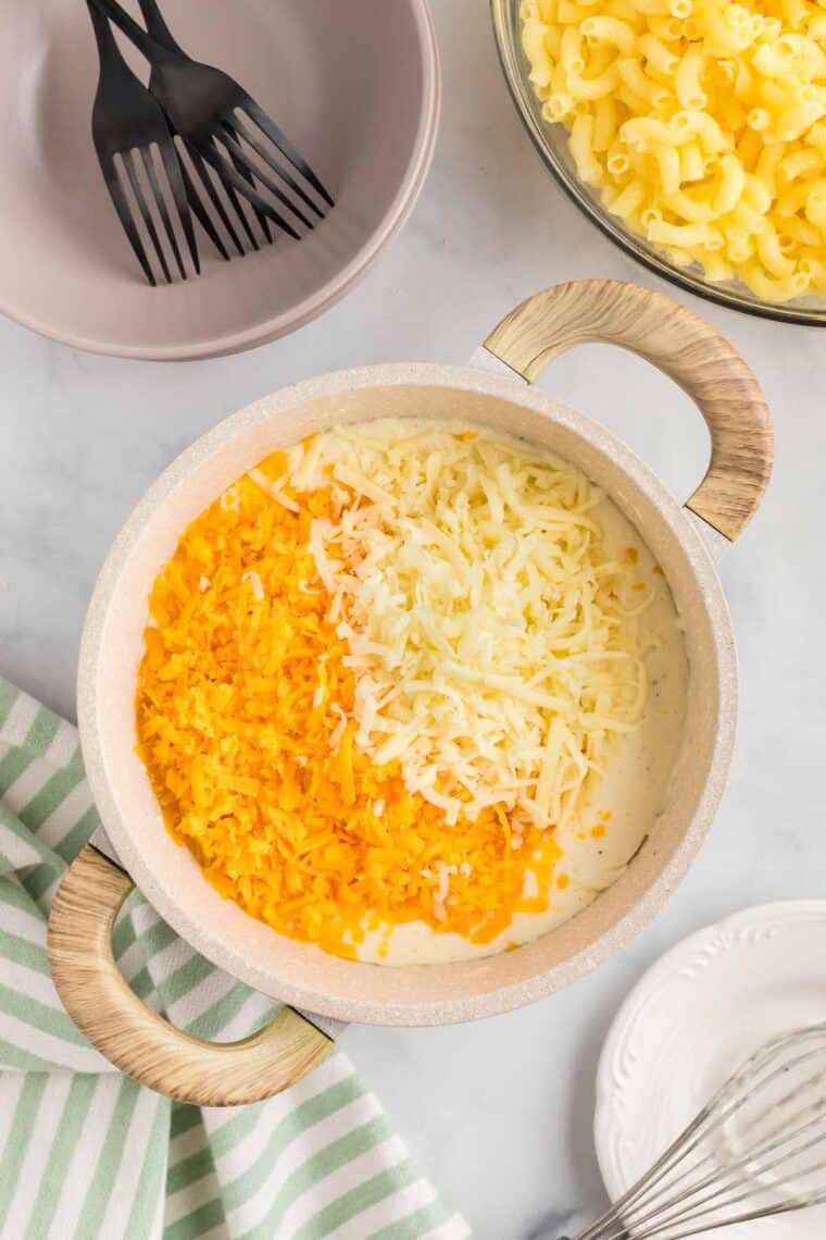 This gluten-free mac and cheese is so creamy and satisfying, with a crunchy breadcrumb topping that takes it over the edge! Adding shredded cheddar and mozzarella cheese to the creamy sauce in a pot.