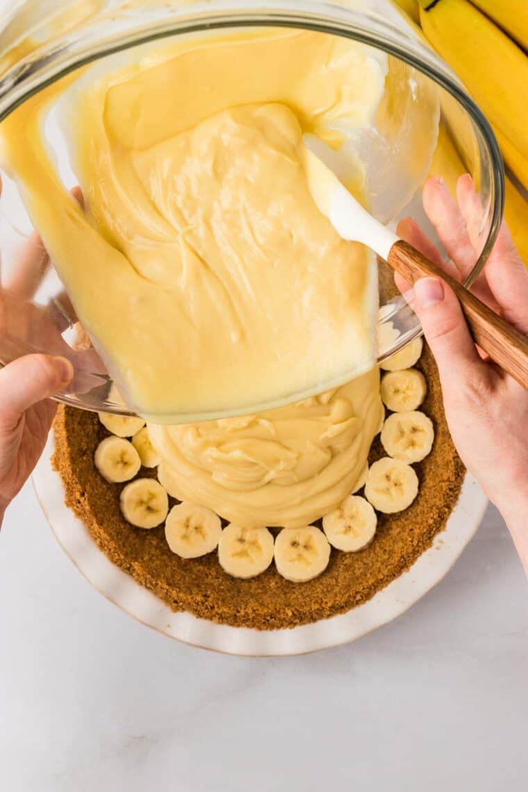 Pouring the filling for banana cream pie over a graham cracker crust lined with banana slices.