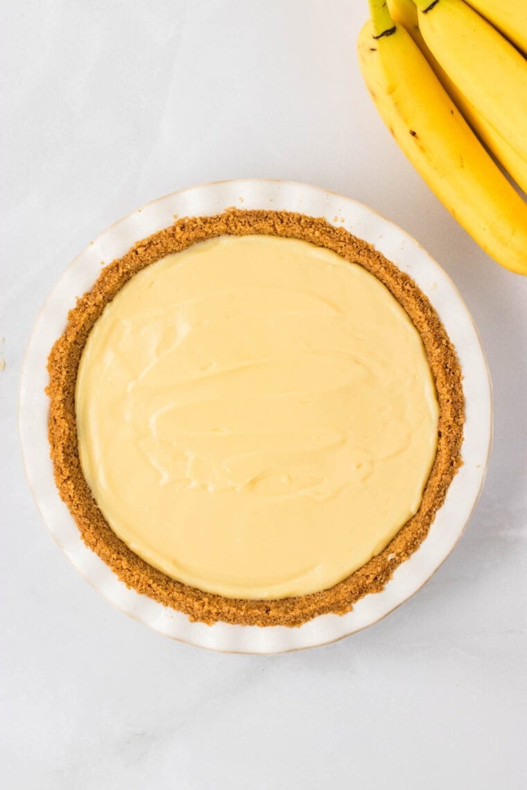 A graham cracker crust lined with banana slices with vanilla pudding spread in a smooth layer over the top.