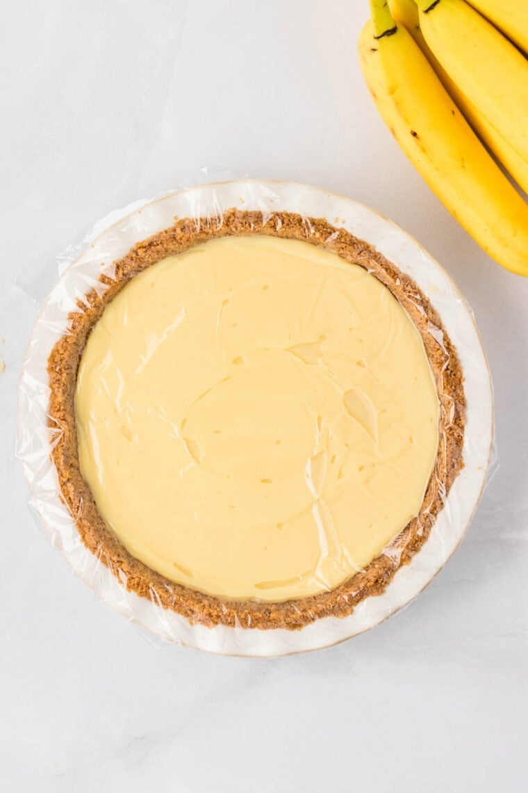 Banana cream pie before adding the whipped cream. Plastic wrap is pressed onto the filling to prevent a film from forming.