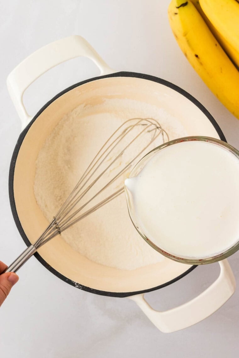 Pouring milk and heavy cream into a mixture of sugar, cornstarch, and salt in a saucepan.