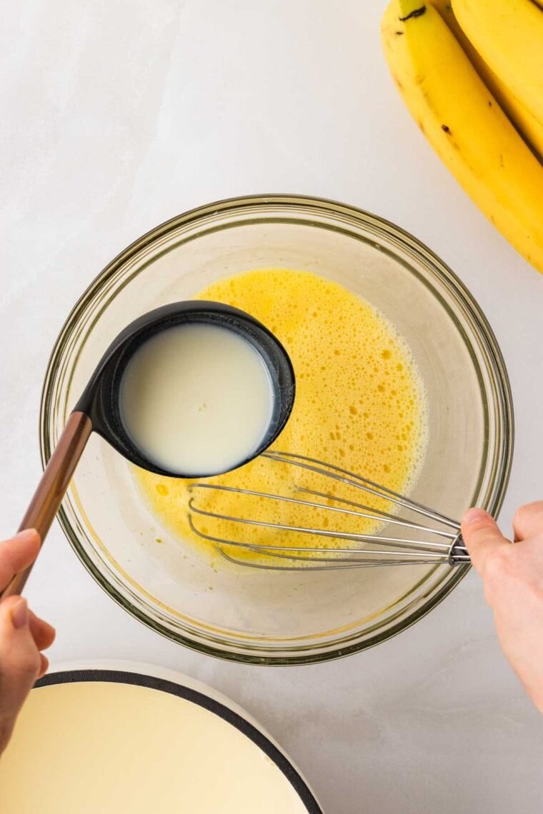 Tempering eggs with a hot mixture of milk, heavy cream, sugar, cornstarch, and salt.