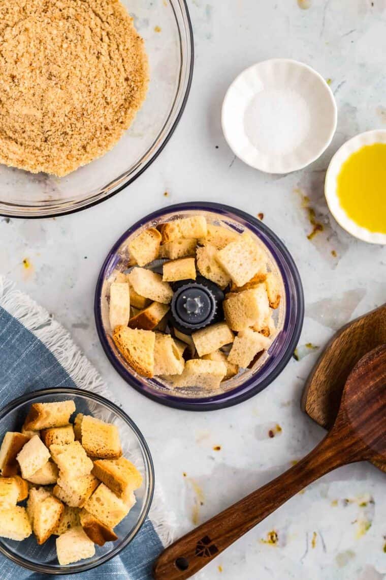 Dried bread cubes in a food processor next to a bowl of breadcrumbs.