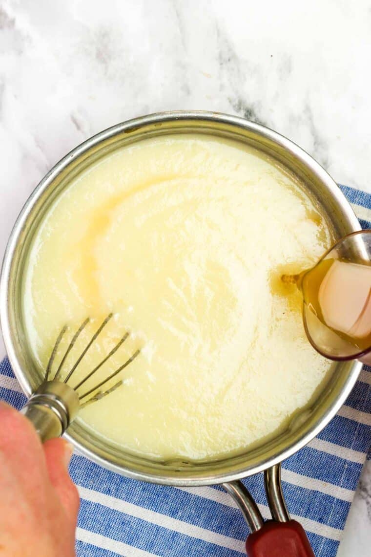 Whisking apple cider vinegar into creamy dressing in a saucepan.