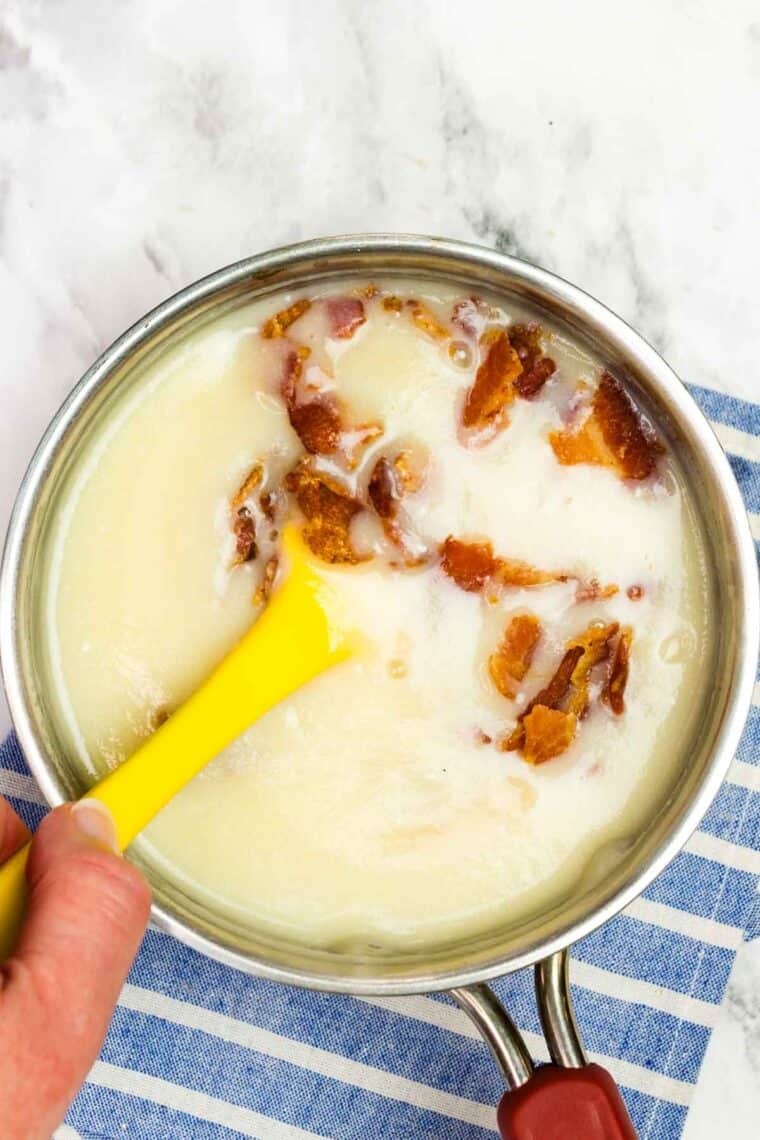 Stirring cooked, crumbled bacon into creamy dressing in a saucepan.