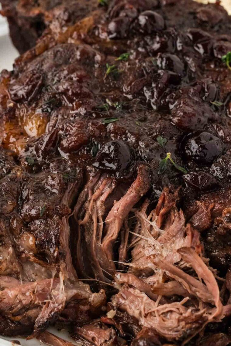 Slow cooker balsamic beef is the answer to your holiday hosting dreams, delivering melt-in-your-mouth beef in a tangy, subtly sweet sauce. Close-up image showing partially shredded slow cooker balsamic beef.