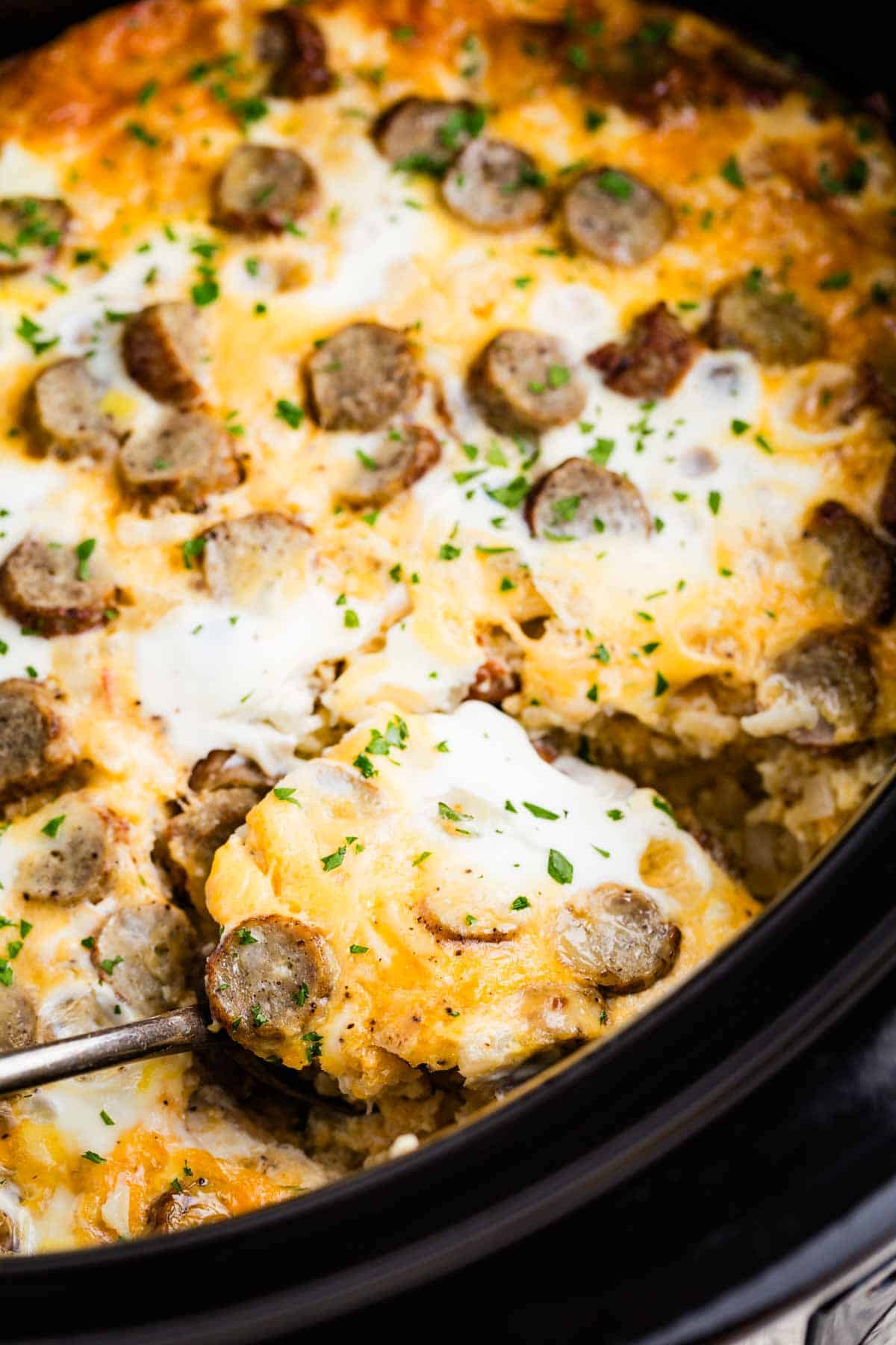 A spoon scooping some cauliflower hash brown casserole out of a slow cooker.