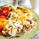 A serving of cauliflower hash brown casserole on a plate with tomato and grapefruit slices.