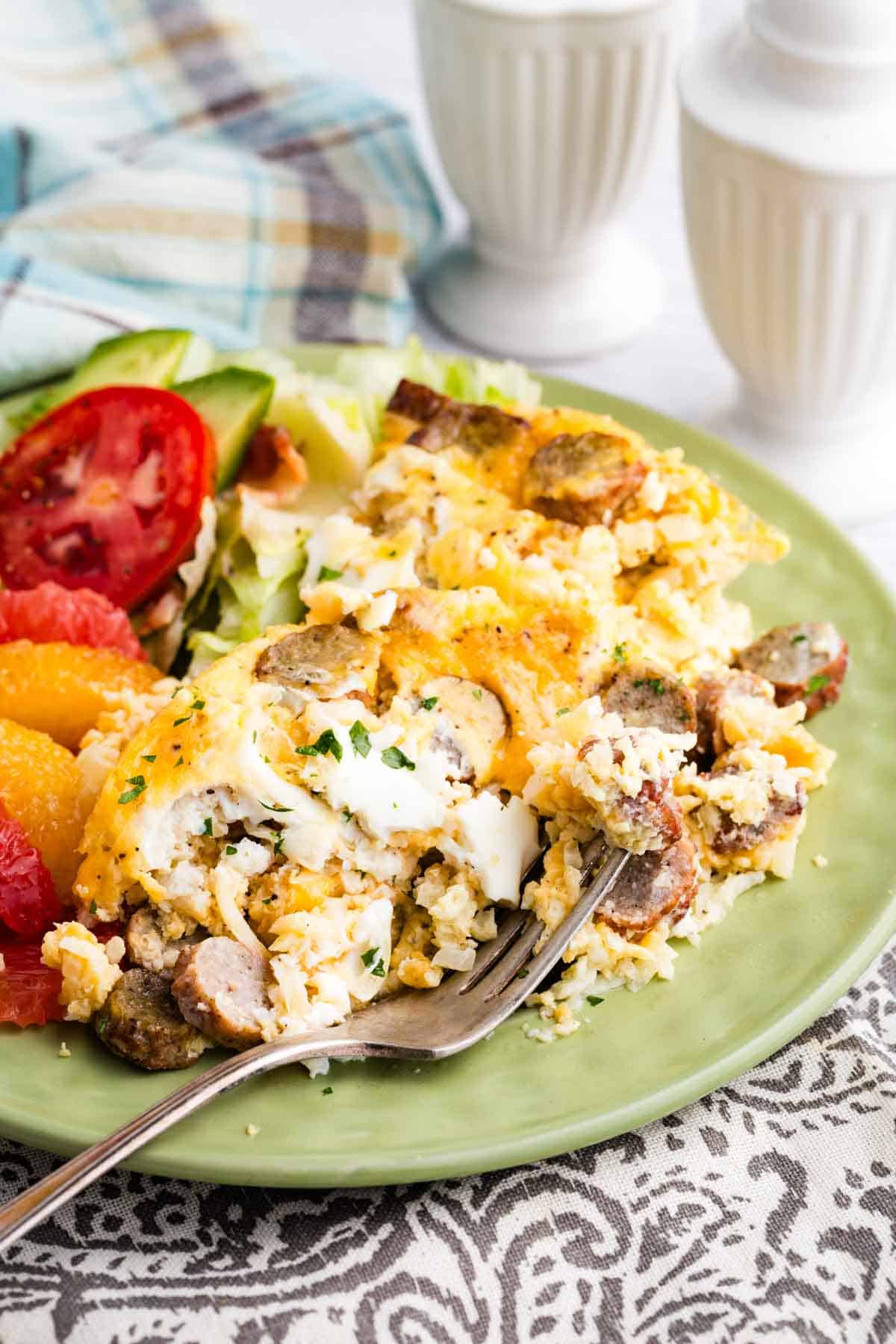 A serving of cauliflower hash brown casserole on a plate with tomato and grapefruit slices.