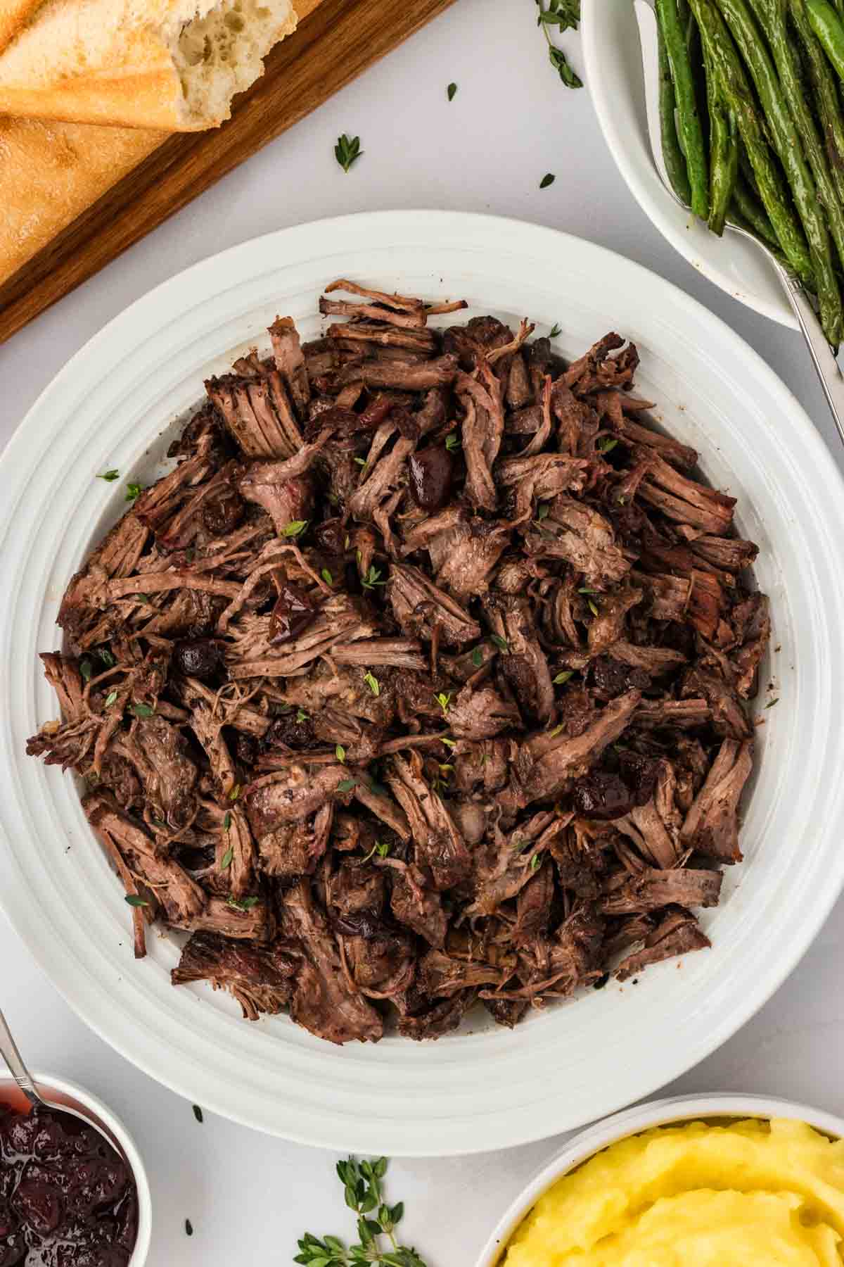 Slow cooker balsamic beef is the answer to your holiday hosting dreams, delivering melt-in-your-mouth beef in a tangy, subtly sweet sauce. Overhead image of a plate loaded with shredded slow cooker balsamic beef.