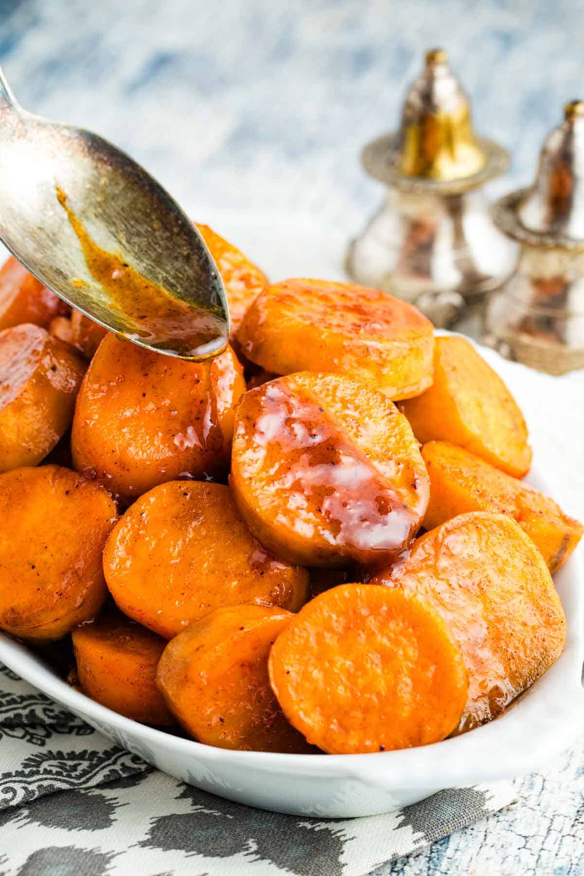 Drizzling brown sugar glaze over candied sweet potatoes in a serving dish.