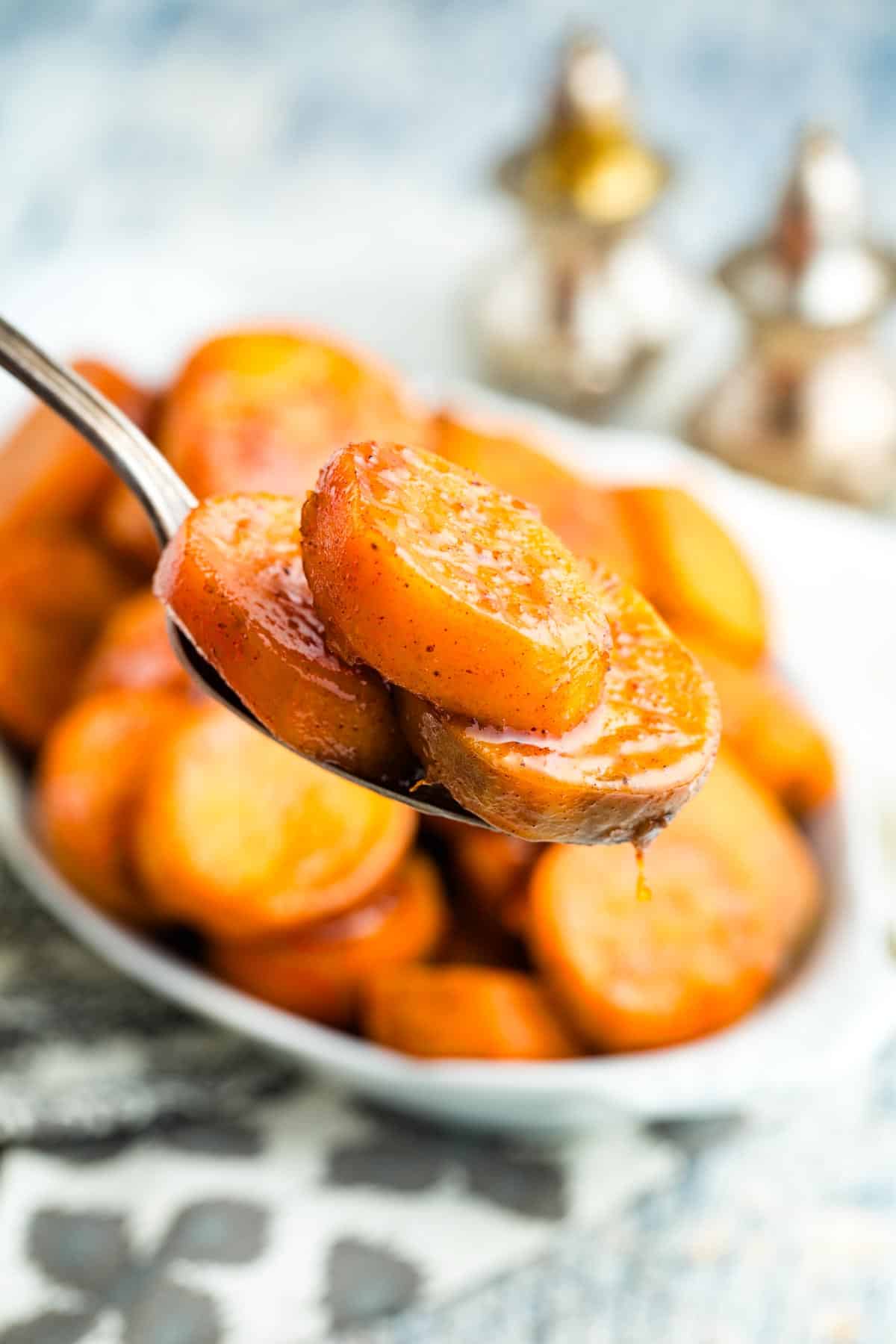 A spoon holding a couple of candied sweet potato slices up to the camera.
