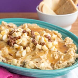 A dish of apple hummus topped with caramel, chopped apples, white chocolate chips, and pecans.